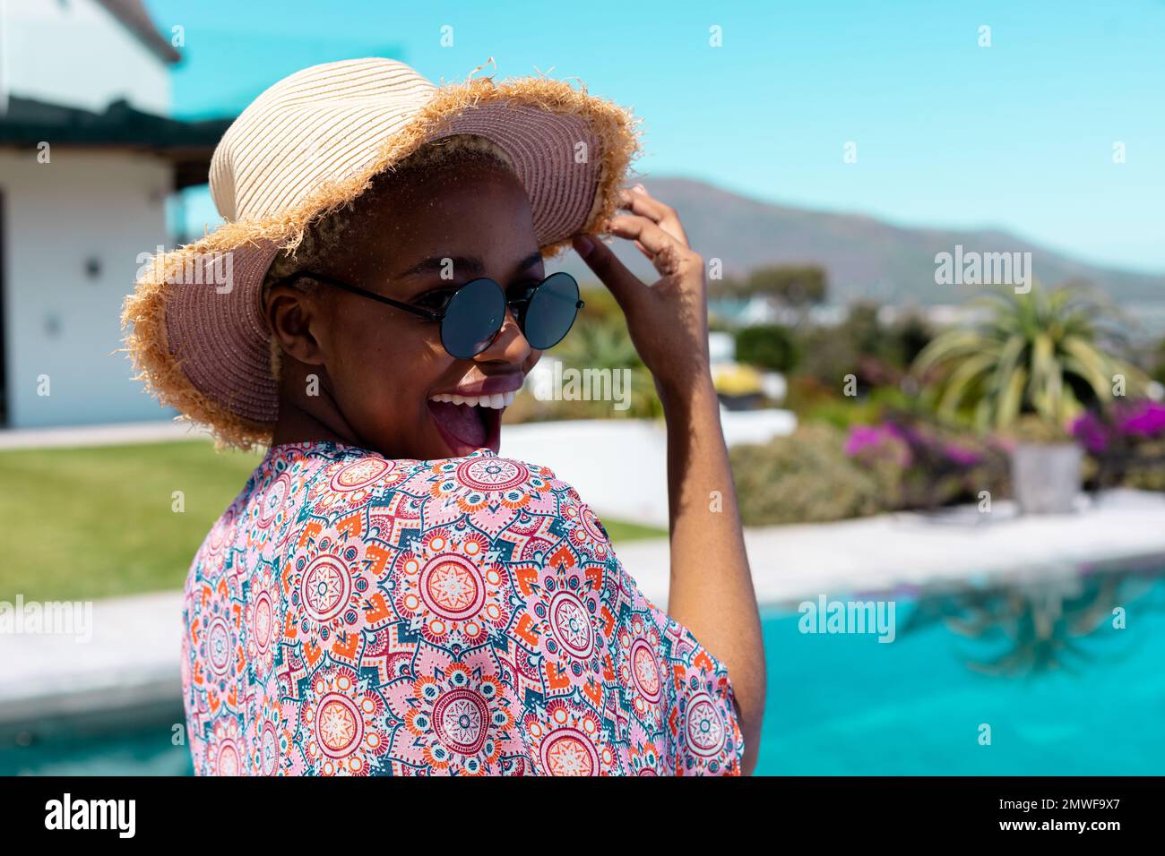 Ritratto di felice ragazza afro-americana che indossa cappello di paglia e occhiali da sole in piscina Foto Stock