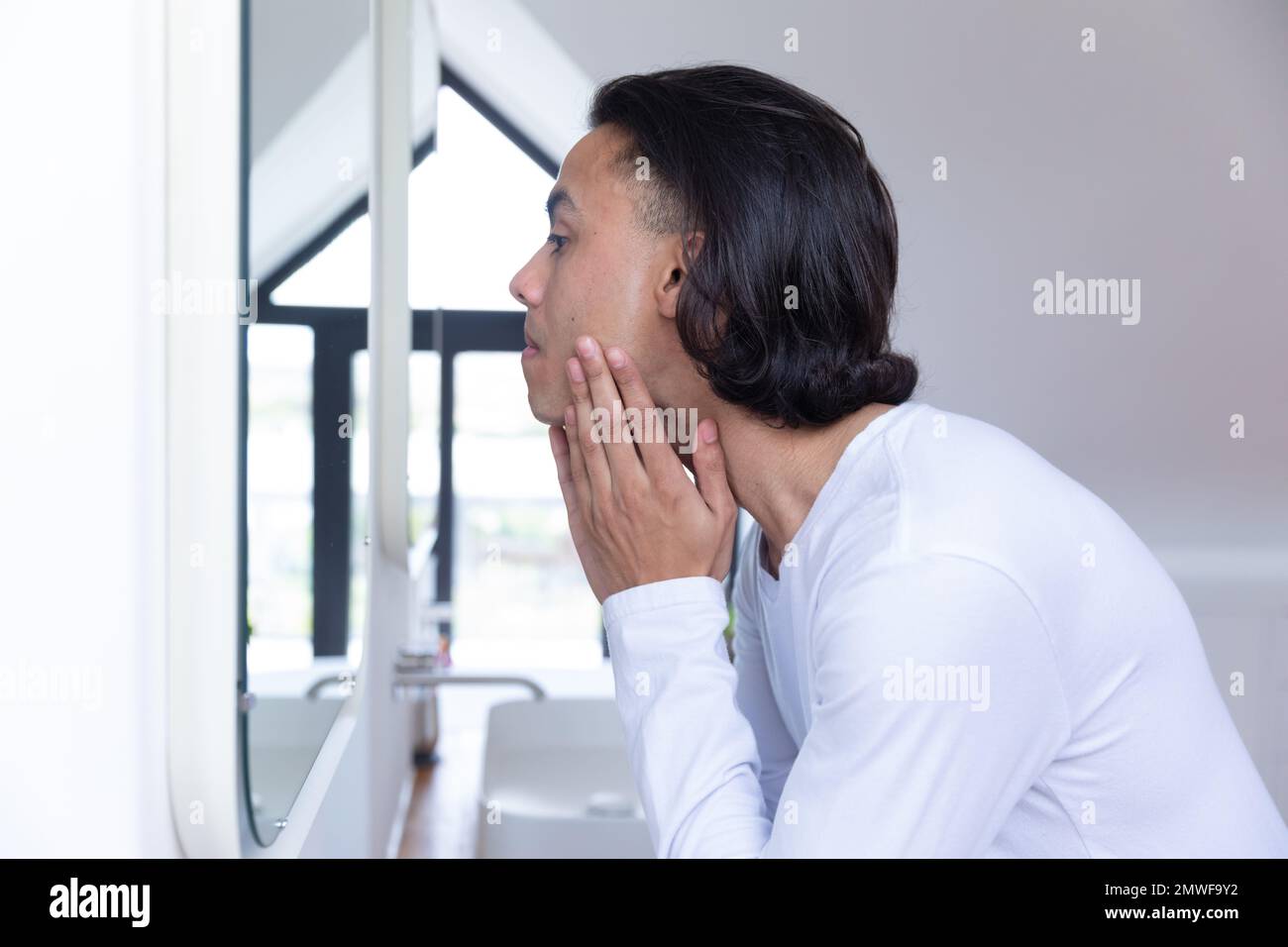 Uomo biraciale che guarda in specchio in bagno Foto Stock