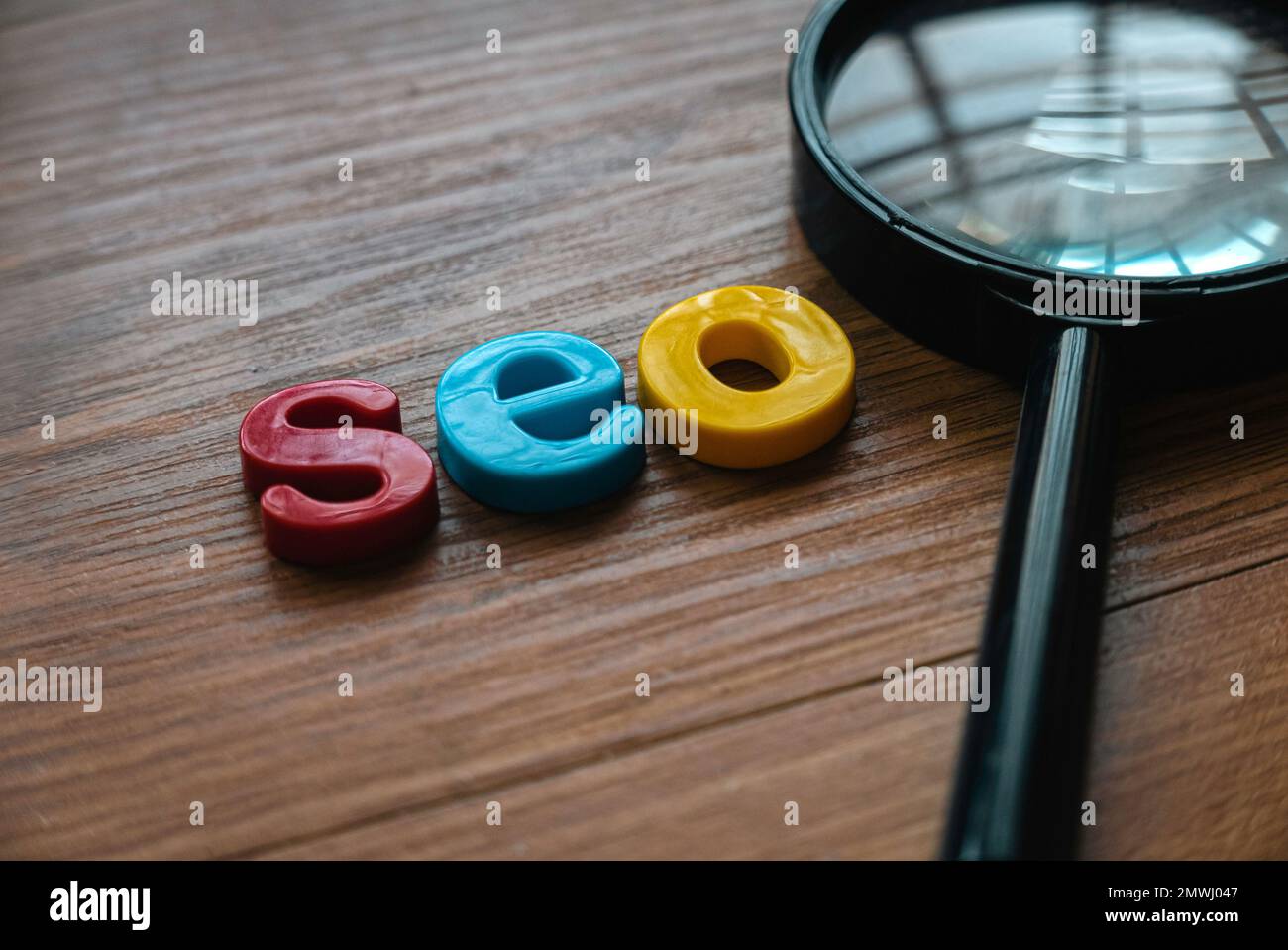 Concetto di ottimizzazione dei motori di ricerca. Lente d'ingrandimento e alfabeto di seo su uno sfondo di legno. Foto Stock