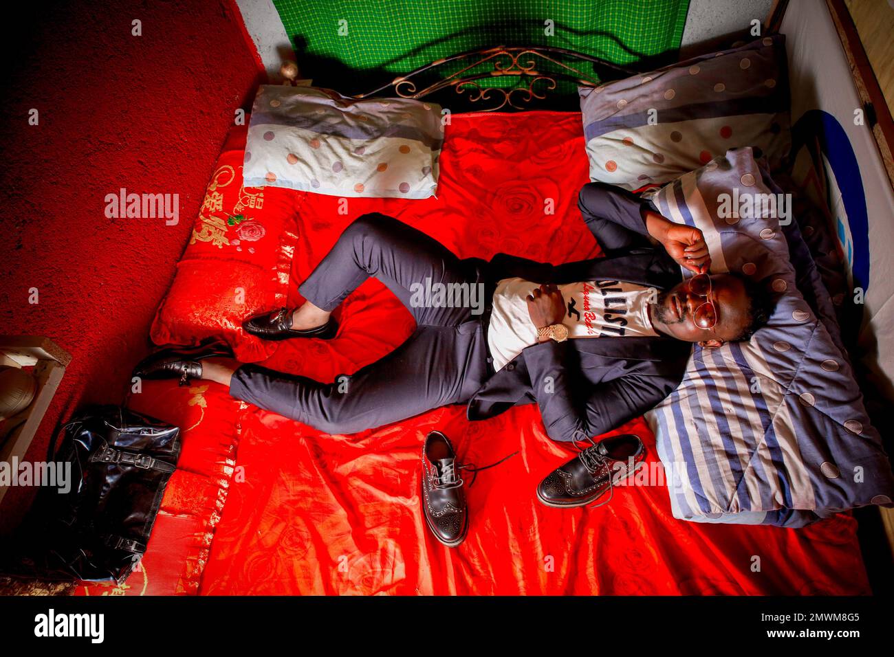 Clinton Chogo, di 23 anni, adagiato sul suo letto all'interno della sua casa dal design colorato vestita con abiti di classe a Kibera. I giovani kenioti sono spinti in una competenza di avere le proprie case lontano dai genitori, dove soprattutto imparano ad affrontare la vita attraverso diverse sfide. La competizione di avere le camere meglio decorate piene di diversi abiti di design è un modo per tenere lontano dalle sfide quotidiane della vita, come l'abuso di droghe, le gravidanze adolescenziali matrimoni precoci, e giudizi negativi da parte della gente del posto. Per la maggior parte dei giovani avere una casa è l'inizio di una nuova vita Foto Stock