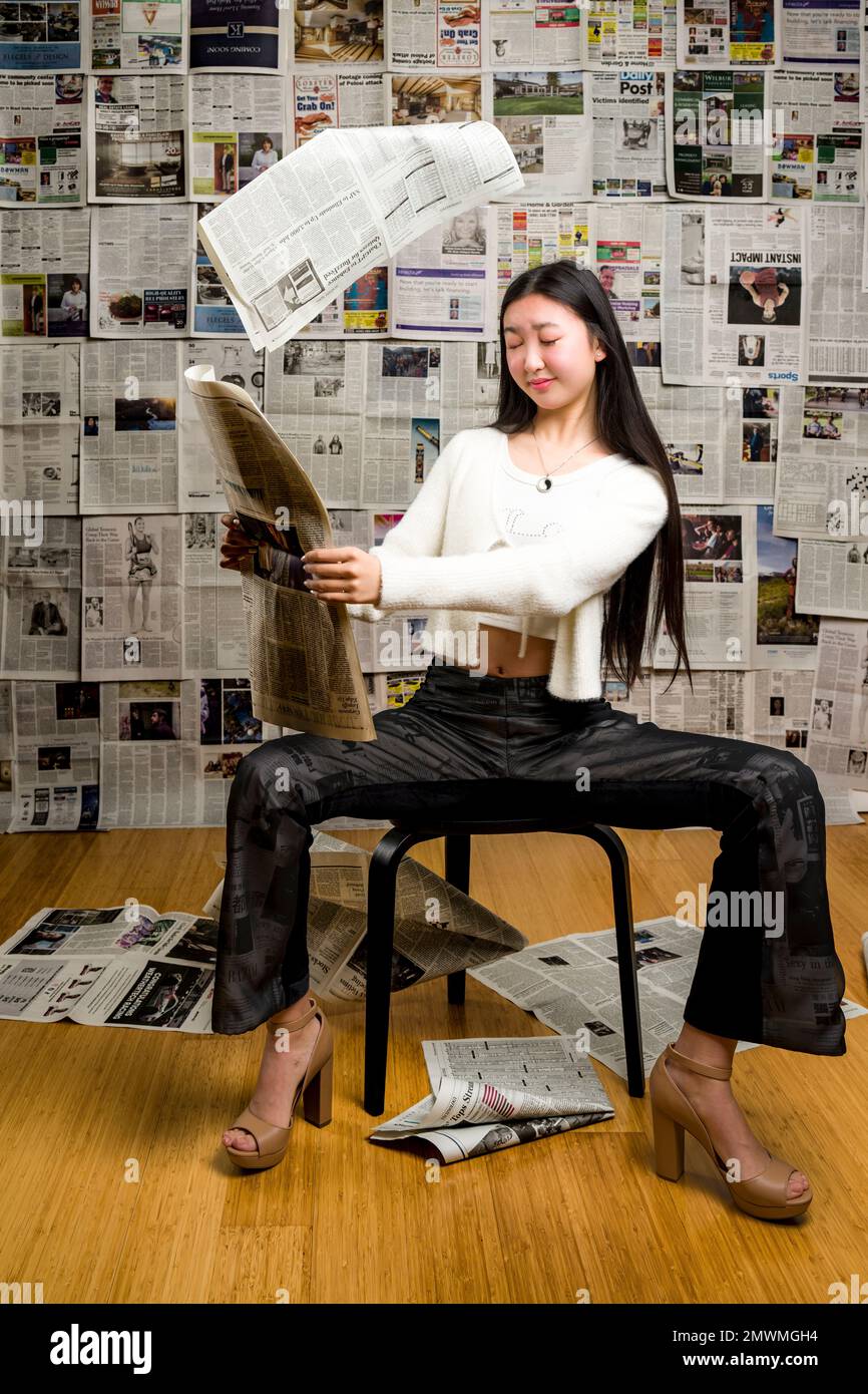 Full Body Tall Teenage Asian Girl seduta davanti allo sfondo dei giornali Foto Stock