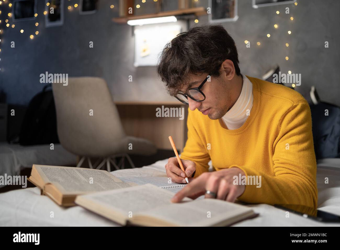 Studente sdraiato su un letto e studiando con attenzione e concentrazione. Giovane che si prepara per l'esame leggendo libri e scrivendo note. Spazio di copia Foto Stock