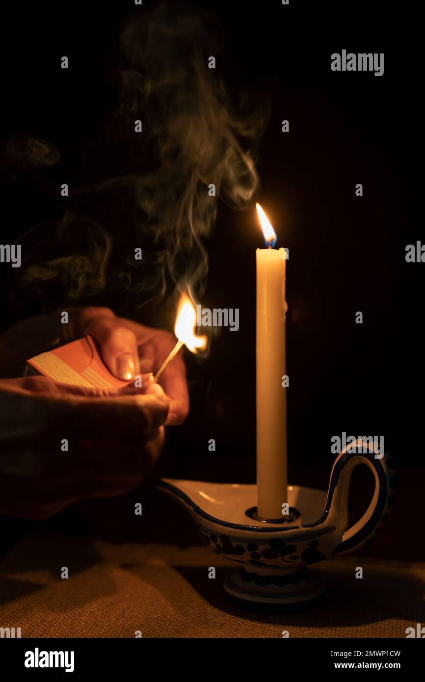 Le mani femminili con un fiammifero bruciante e smoldering, vicino ad una candela che brucia nel portacandele Foto Stock