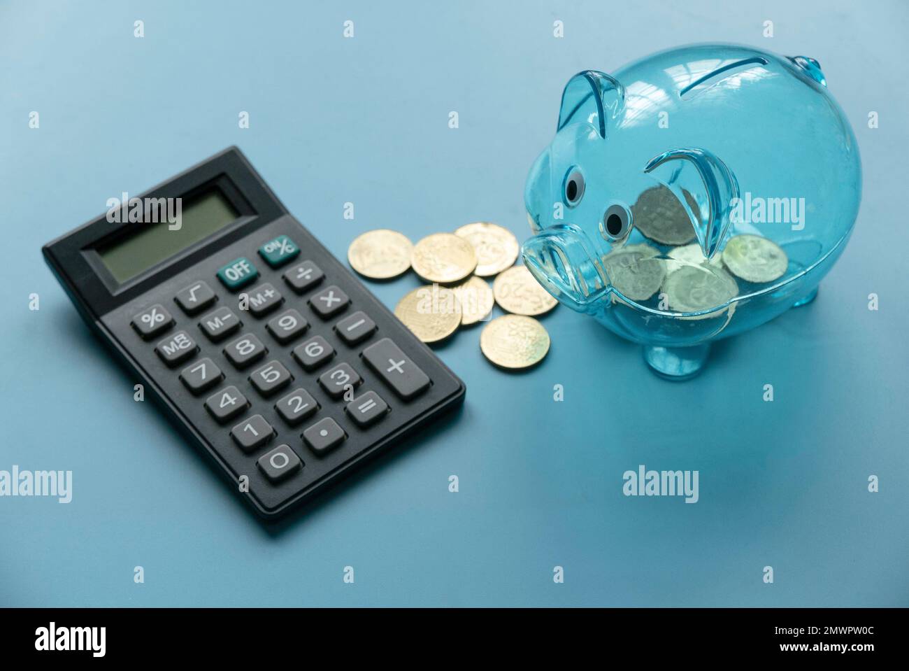 Concetto di business, finanza, investimento, risparmio e finanziamento. Banca di porcellini trasparente, monete e calcolatrice su sfondo blu. Foto Stock