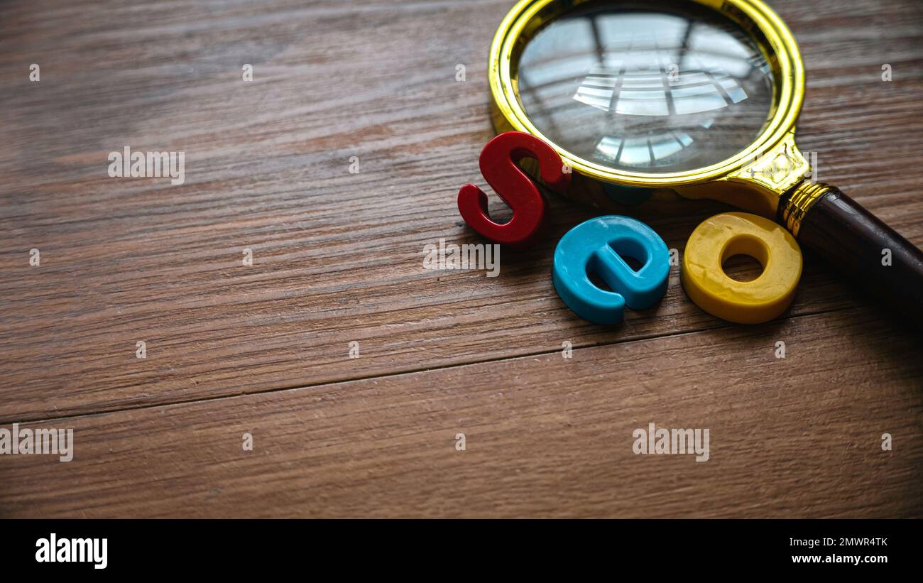 Concetto di ottimizzazione dei motori di ricerca. Lente d'ingrandimento e alfabeto di seo su uno sfondo di legno. Foto Stock
