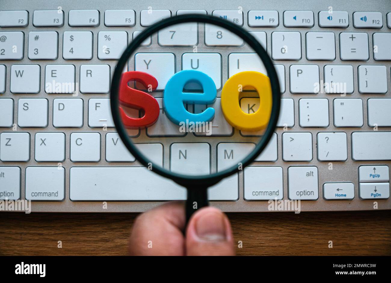 Concetto di ottimizzazione dei motori di ricerca. Una mano che tiene la lente d'ingrandimento ingrandire una parola seo su una tastiera del computer. Foto Stock
