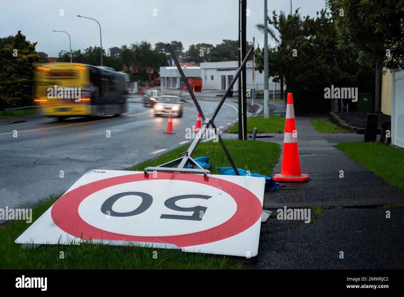 50km segnale di limite di velocità soffiato dal vento. Auto fuori fuoco che viaggiano su strada. Auckland dopo la tempesta. Foto Stock