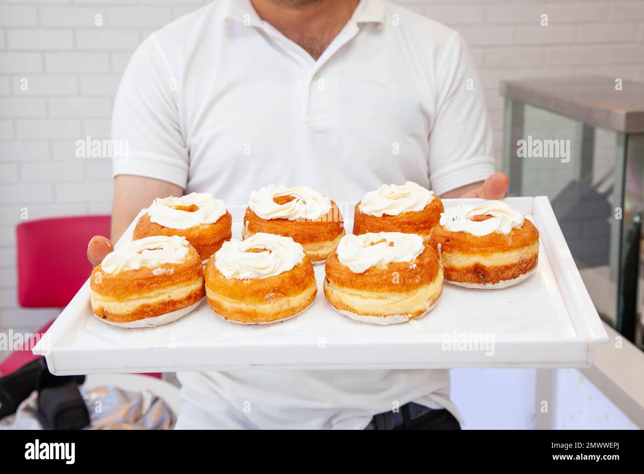 Cuoco del forno mostra la scatola delle ciambelle brioche appena fatte su un vassoio bianco Foto Stock