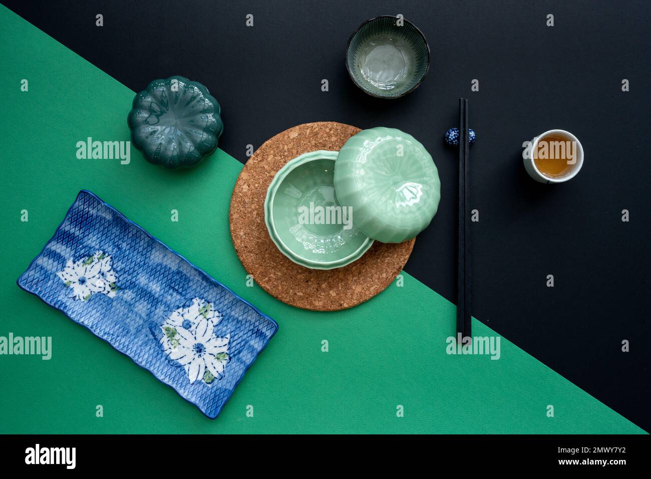 Tavolo giapponese o cinese con tradizionale tappeto da tavolo e stoviglie con sfondo verde e nero. Concetto di mangiare, mangiare, mangiare e bere. Foto Stock