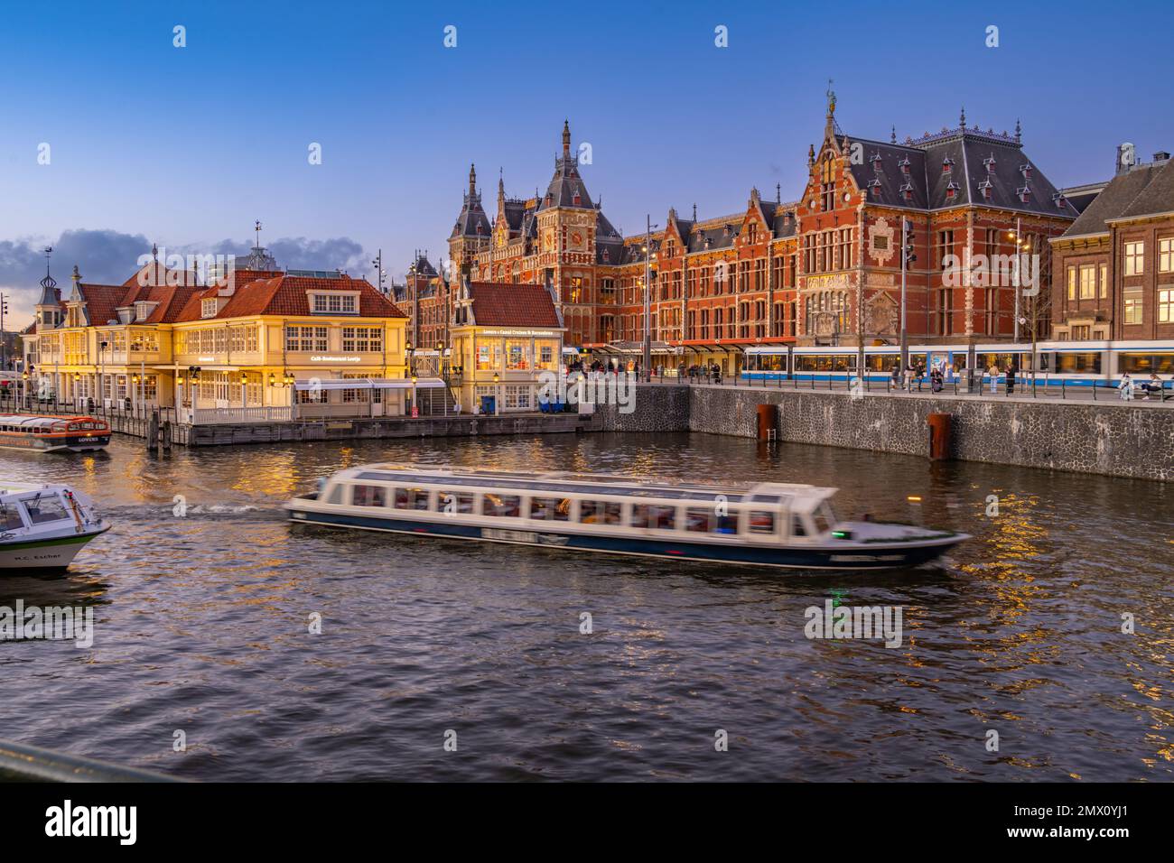 La parte anteriore della stazione centrale di Amsterdam IJzijde dall'altra parte del porto da via Prins Hendrikkade al crepuscolo Foto Stock