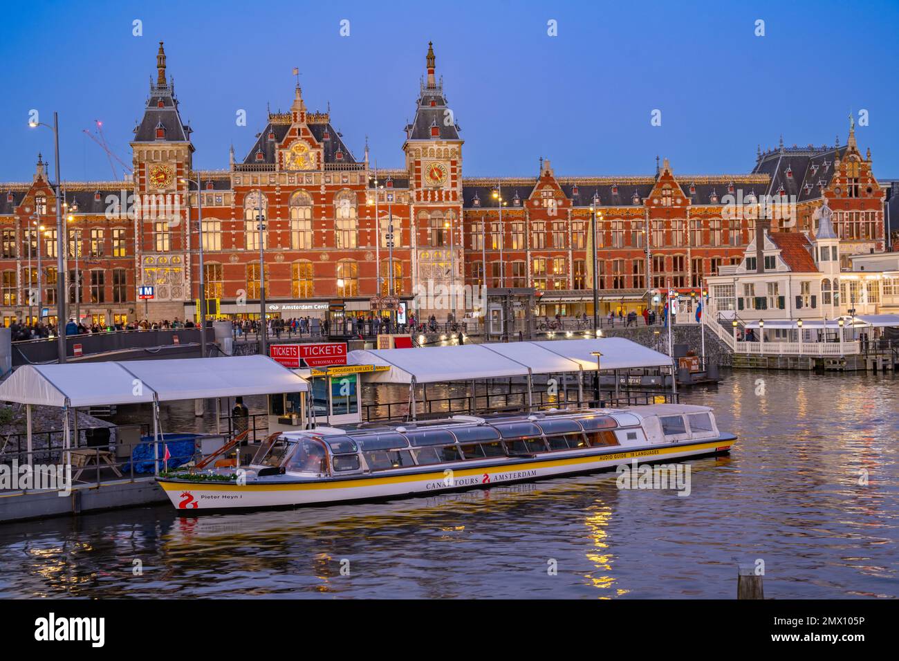 La parte anteriore della stazione centrale di Amsterdam IJzijde dall'altra parte del porto da via Prins Hendrikkade al crepuscolo Foto Stock