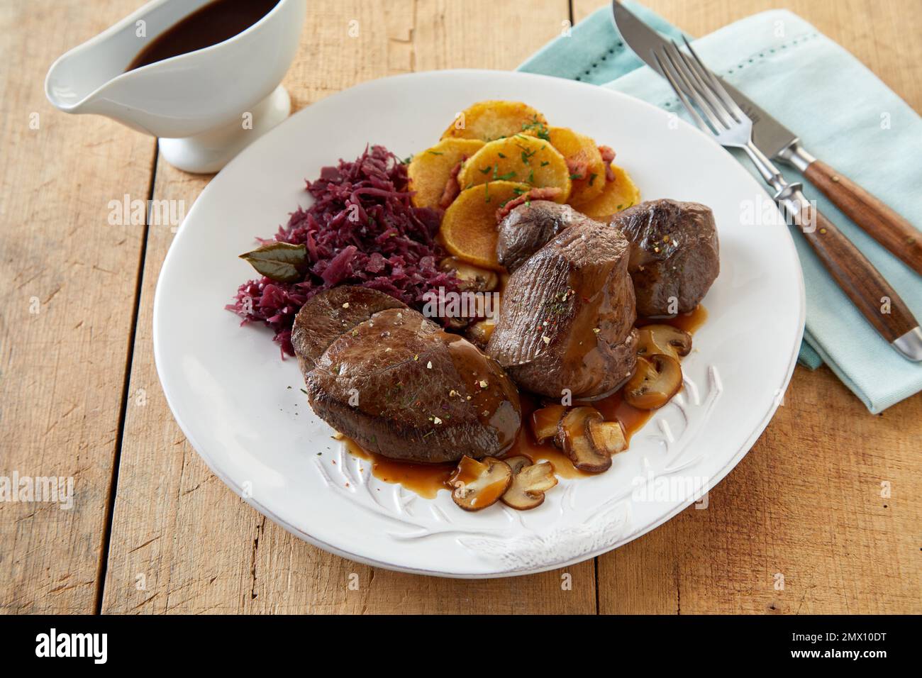 Dall'alto delizioso cervo con crauti e patate servito su piatto vicino alla barca salsa e utensili sul tavolo da ristorante in legno Foto Stock