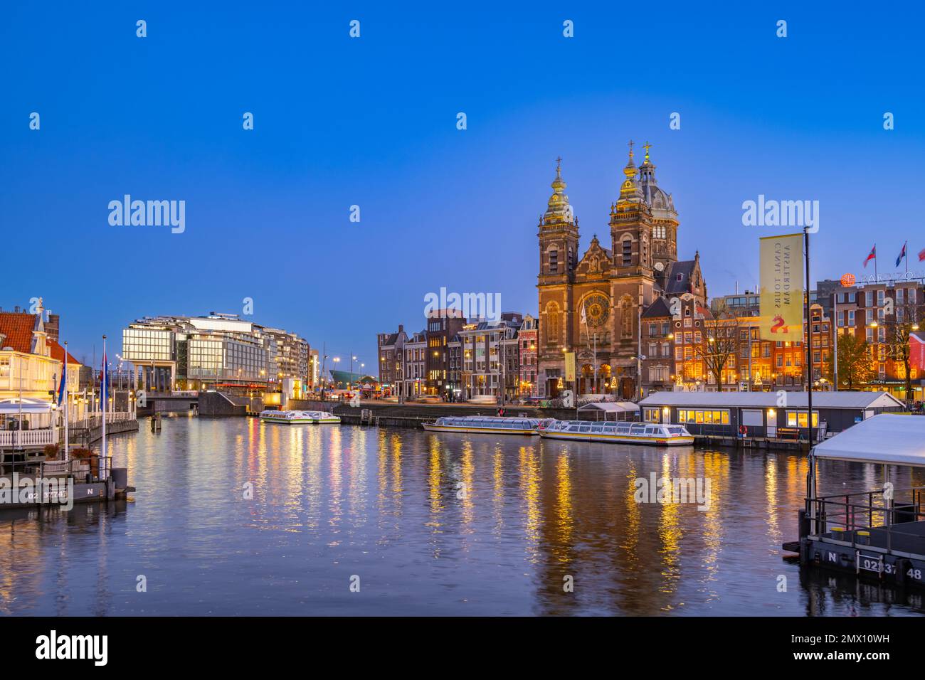 Guardando attraverso il porto dalla stazione centrale IJzijde, attraversate il porto verso la chiesa di San Nicola e Prins Hendrikkade Street al crepuscolo Foto Stock