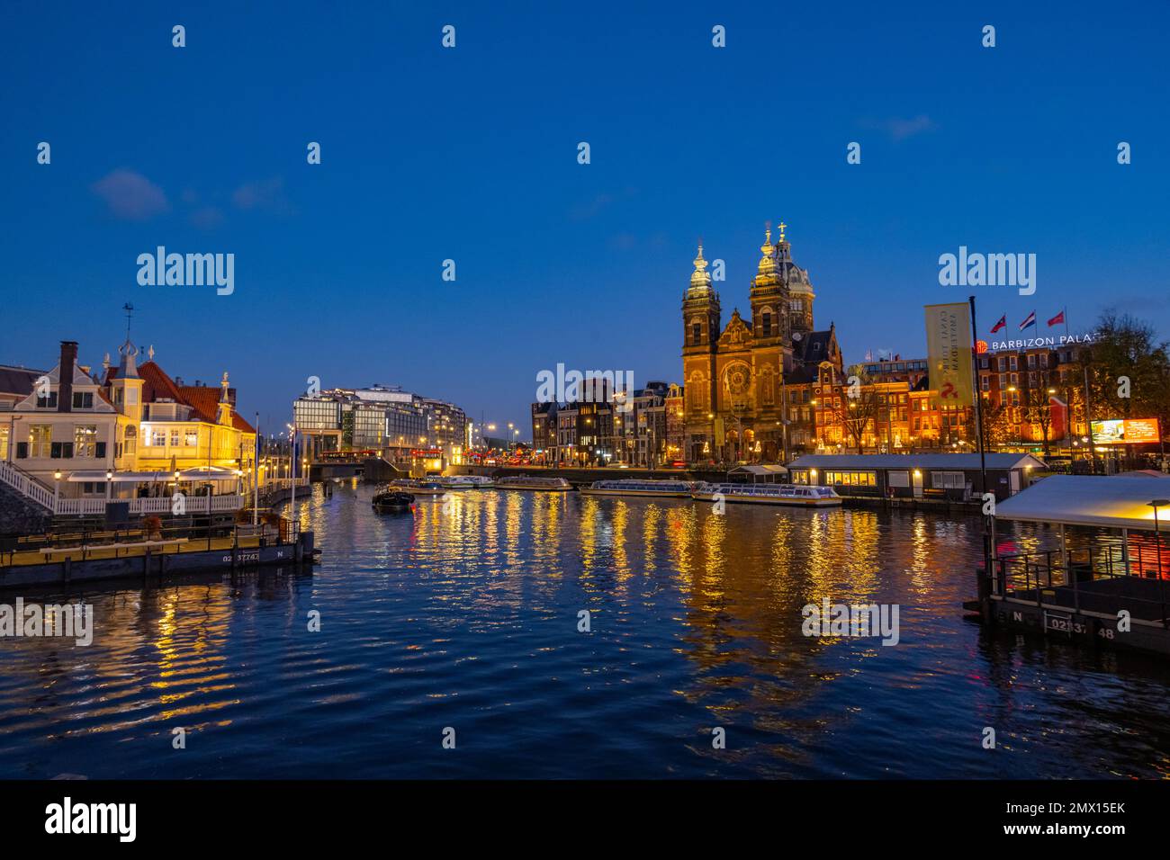 Guardando attraverso il porto dalla stazione centrale IJzijde, attraversate il porto verso la chiesa di San Nicola e Prins Hendrikkade Street al crepuscolo Foto Stock