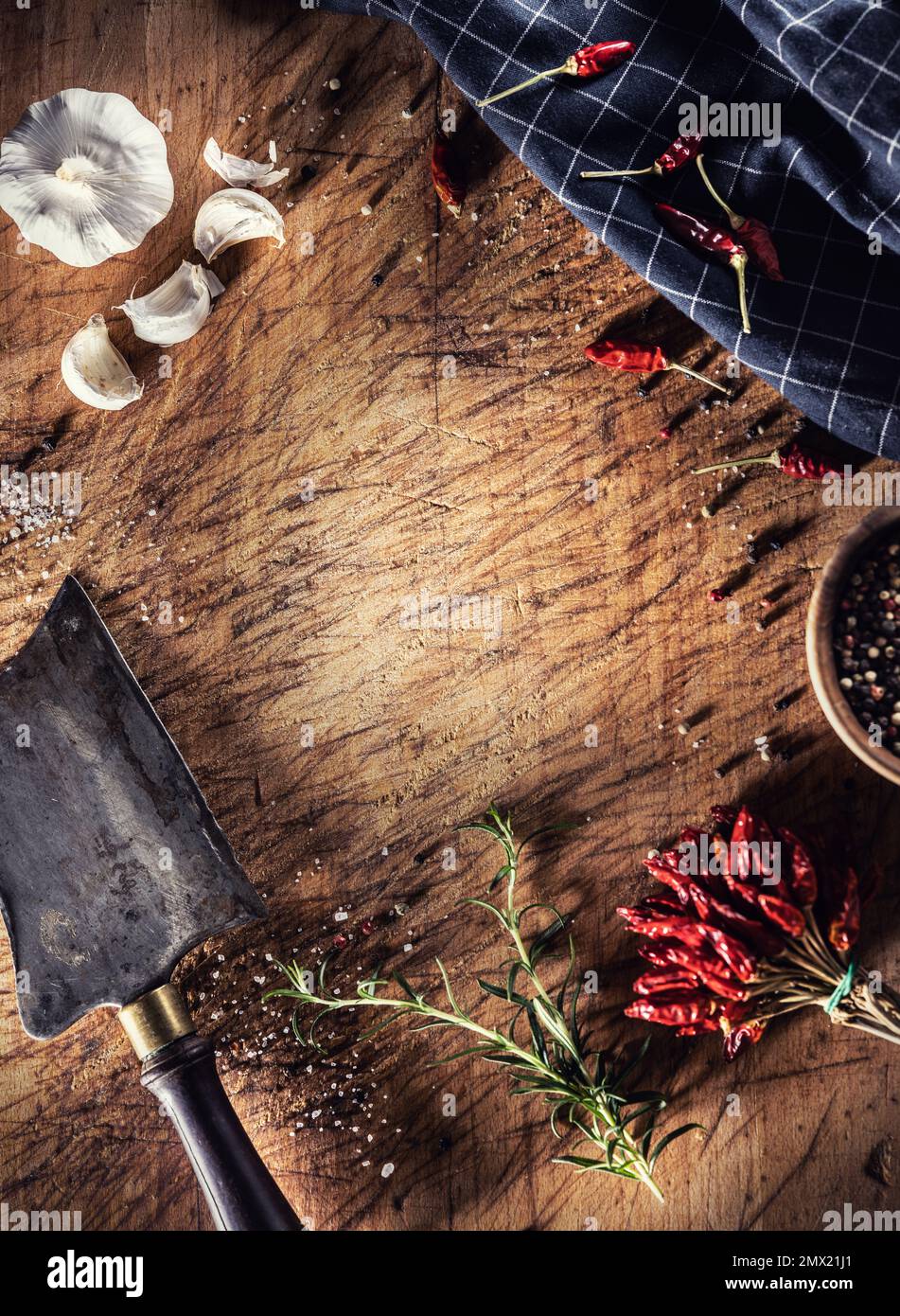Un vecchio tagliere con una scagliatrice di macellaio, pepe, peperoncino, aglio, sale e rosmarino su di esso - Top of view. Foto Stock