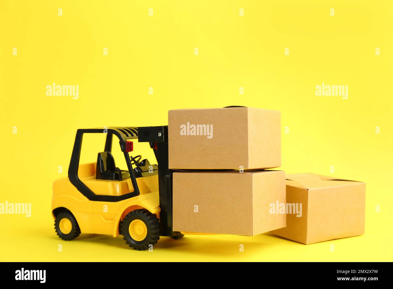Modello di carrello elevatore e scatole di cartone su sfondo giallo. Servizio di corriere Foto Stock