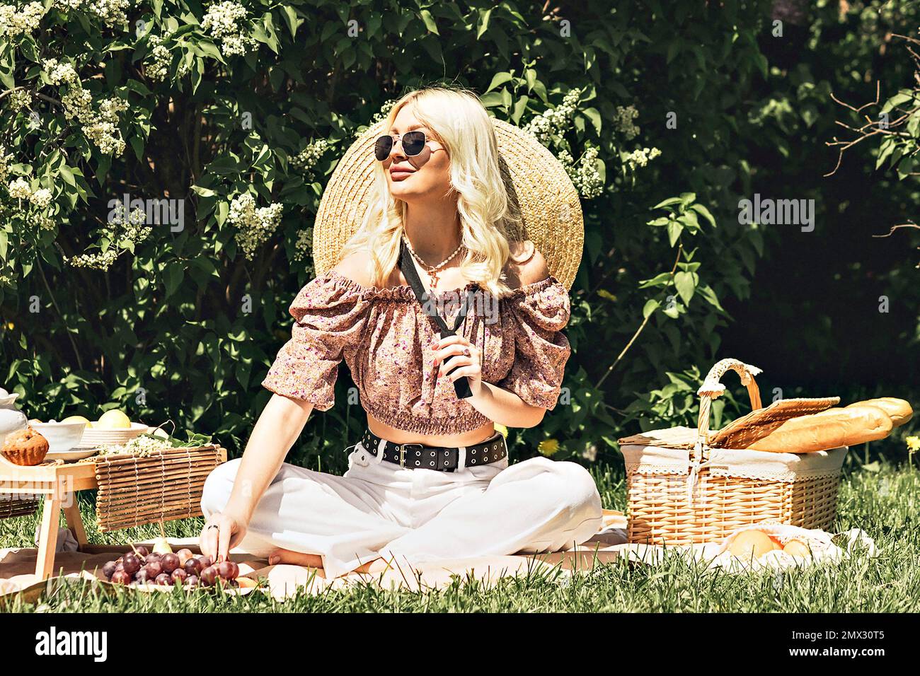 Foto di una bella bella ragazza bionda carina che tiene in mano una fragola. Attività ricreative all'aperto, picnic estivo. Foto Stock