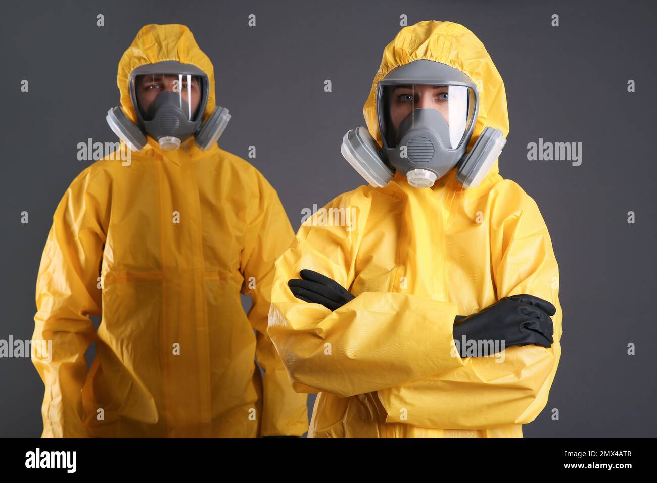 Uomo e donna che indossano tute di protezione chimica su sfondo grigio. Ricerca sui virus Foto Stock