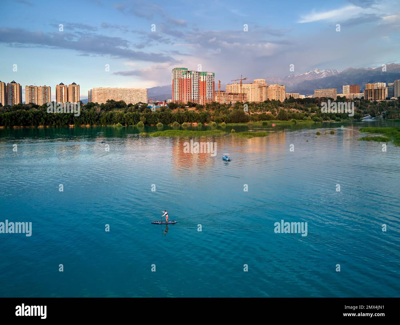 Top Down drone aereo colpo di uomo a stand up paddle board SUP nel fiume e lago di montagna Sairan in città Almaty al tramonto in Kazakistan. Foto Stock