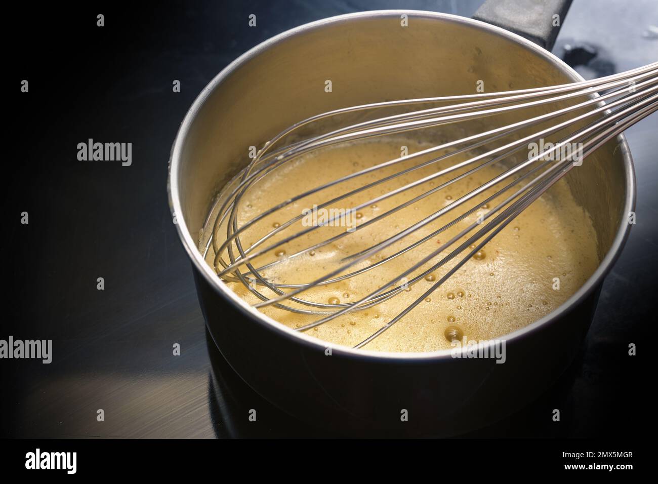 Preparazione della salsa di frittura, la miscela di uova è mescolata a bassa temperatura fino a schiumoso in una pentola di acciaio su un piano cottura nero, concetto di cottura, spazio di copia Foto Stock