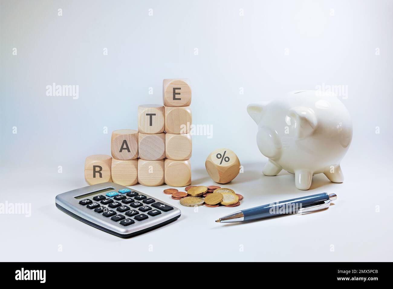Calcola con interesse variabile, cubi di legno con il tasso di parola e un segno di percentuale, piggy bank, calcolatrice e alcune monete su uno sfondo grigio chiaro Foto Stock