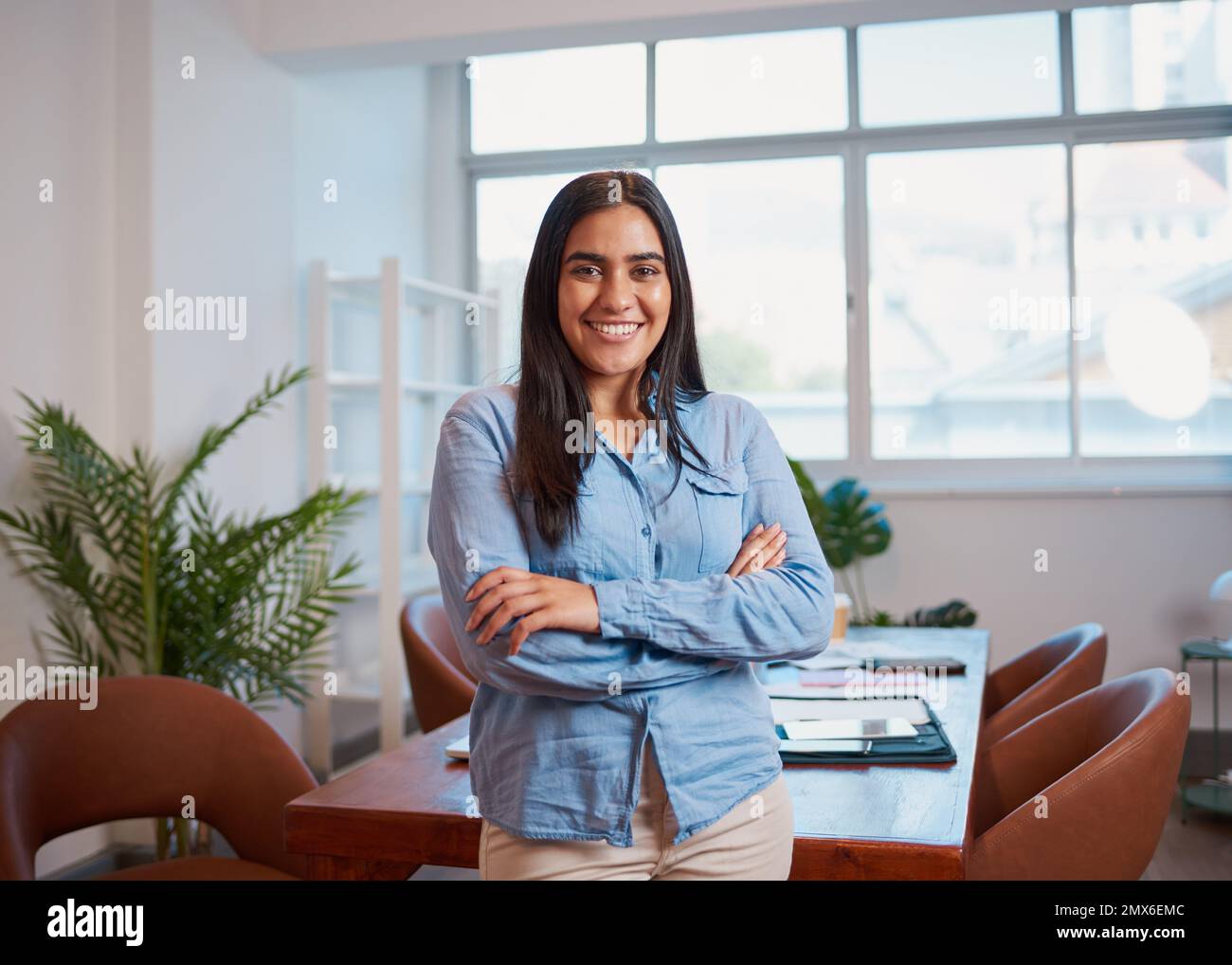 Giovane donna indiana si alza in braccia da ufficio ripiegate, moderne piante da sala riunioni Foto Stock