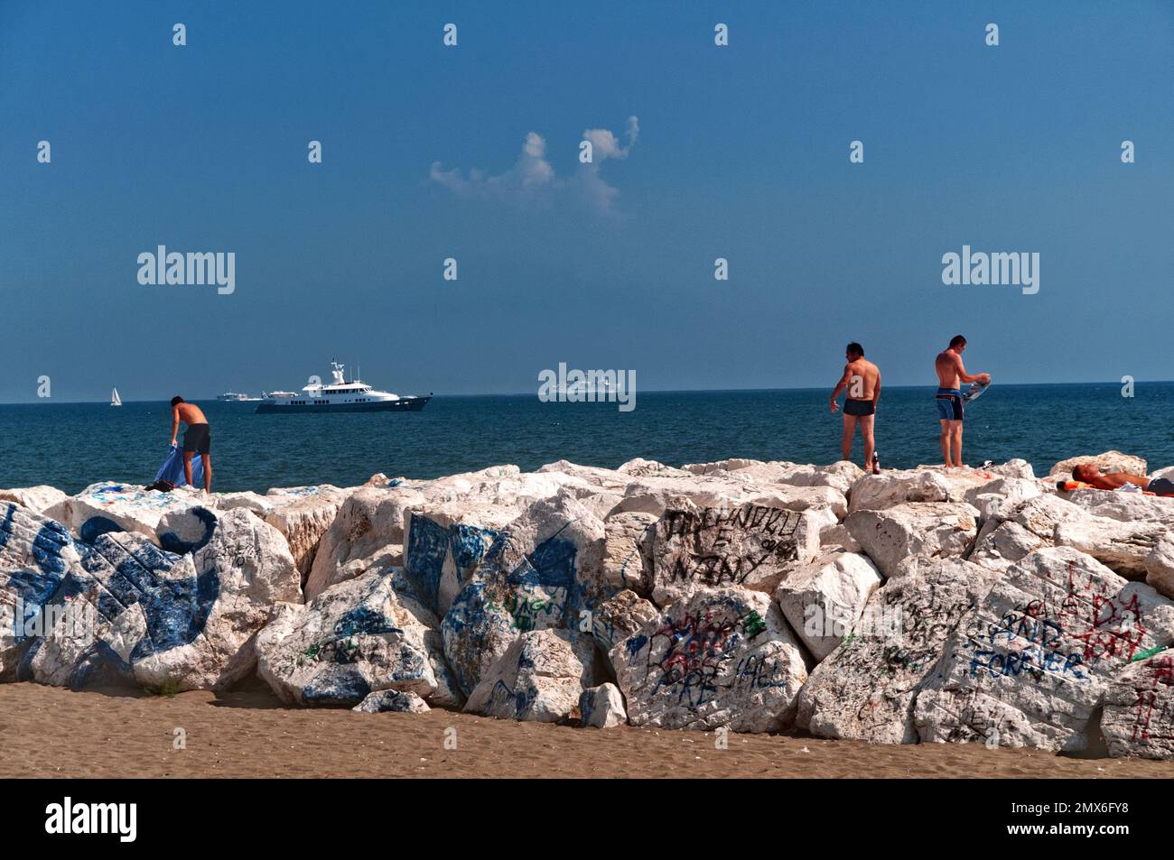 Tre giovani uomini in piedi su grandi rocce a Mappatella Beach a Napoli, Italia Foto Stock