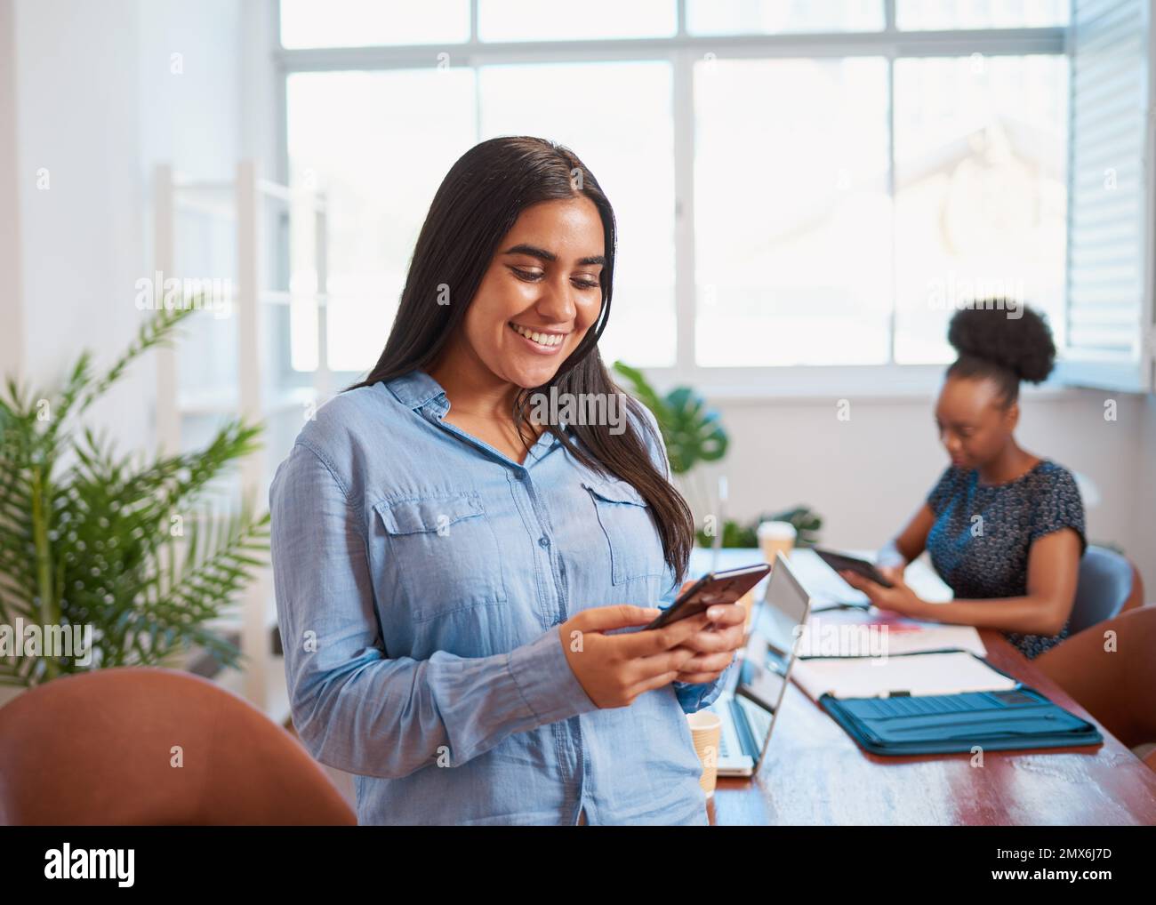 Giovane donna d'affari che usa il cellulare, collega nello spazio ufficio della sala riunioni Foto Stock