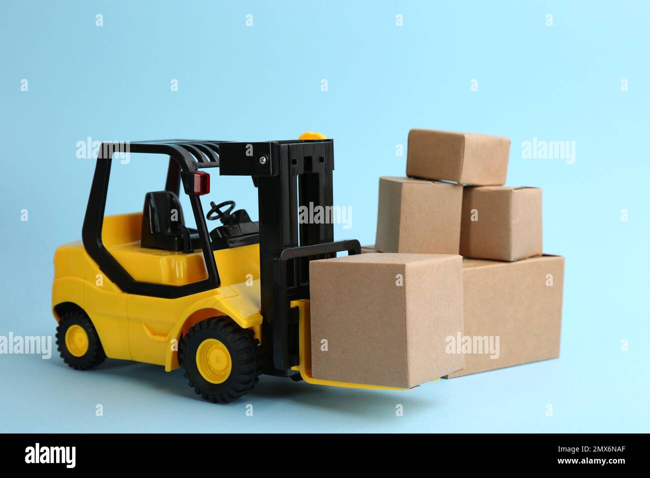 Modello di carrello elevatore a forche e scatole di cartone su sfondo azzurro. Servizio di corriere Foto Stock