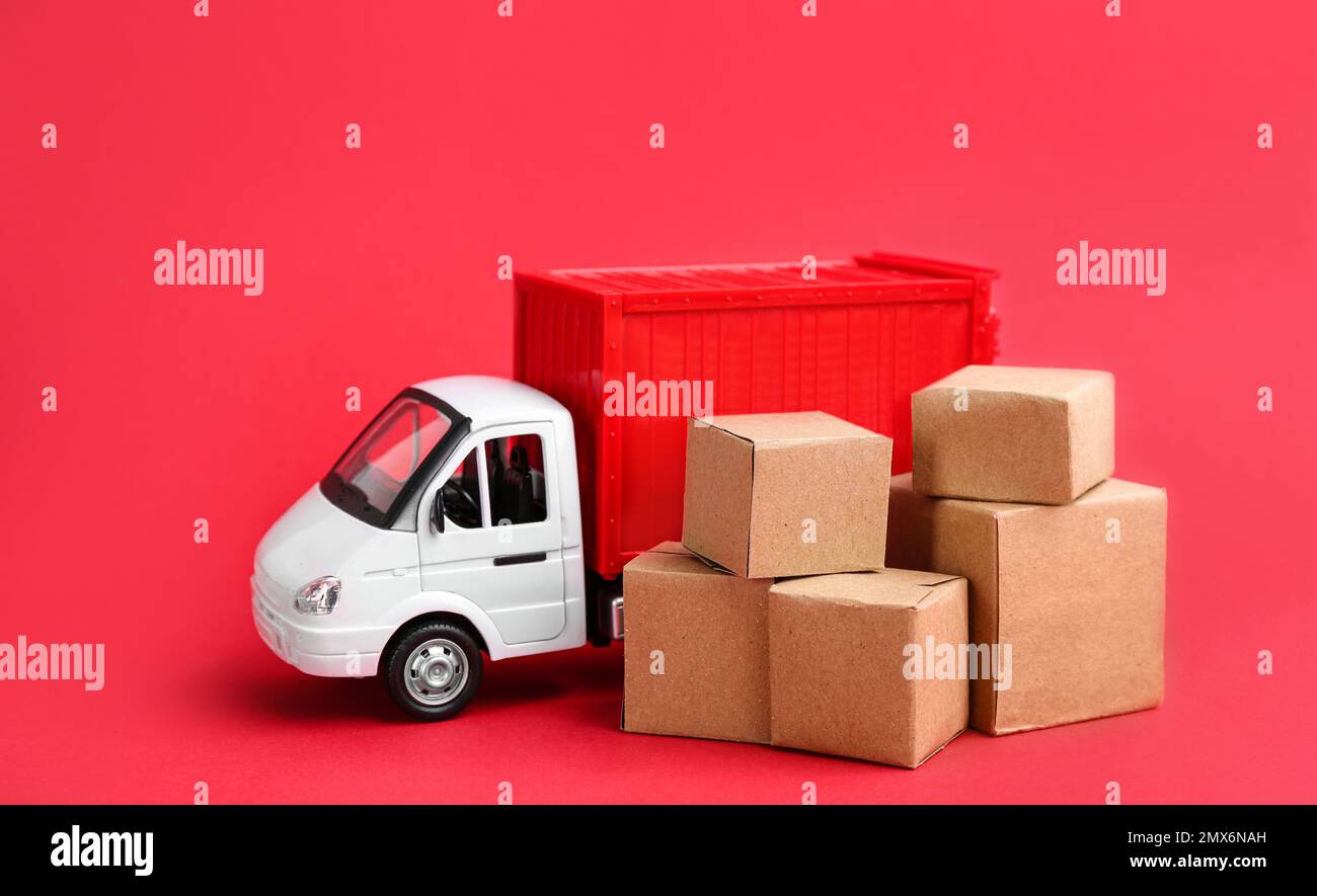 Modello di carrello e scatole di cartone su sfondo rosso. Servizio di corriere Foto Stock