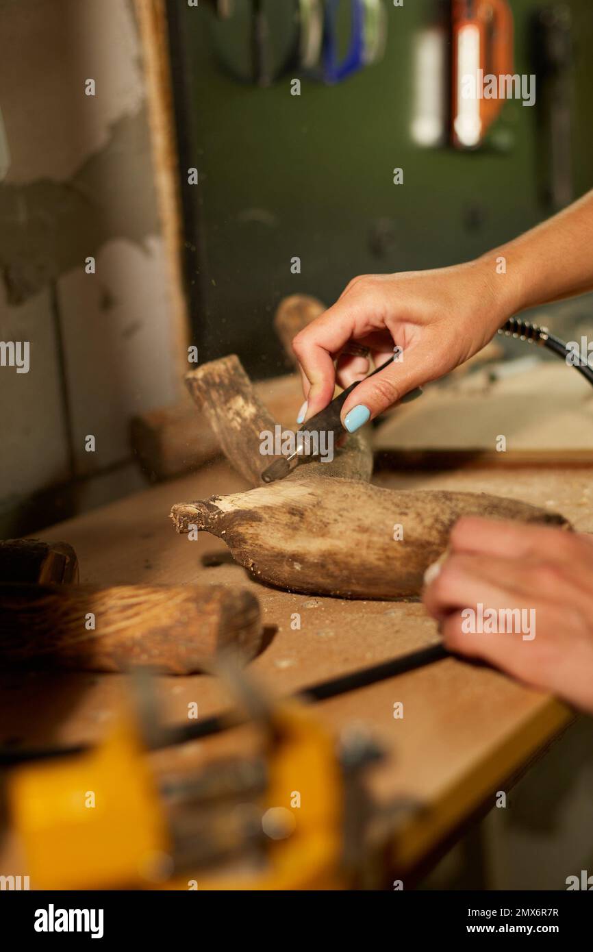 Donna che usa il potere di legno strumenti di lavoro innesto, scultura mentre la creazione, creazione artigianato souvenir fatti a mano, donna in officina. Foto Stock