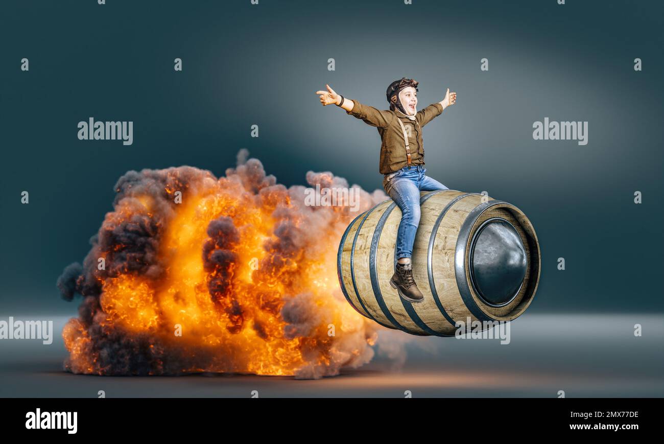 bambino vestito da aviatore su un barile volante con fiamme e fumo Foto Stock