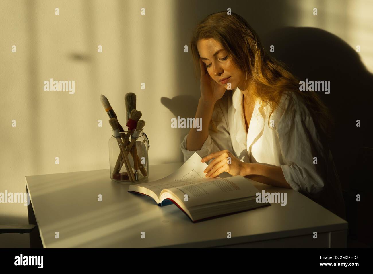 Una ragazza che legge un libro nella stanza al tavolo, alla luce del sole. Tempo libero. Foto di alta qualità Foto Stock