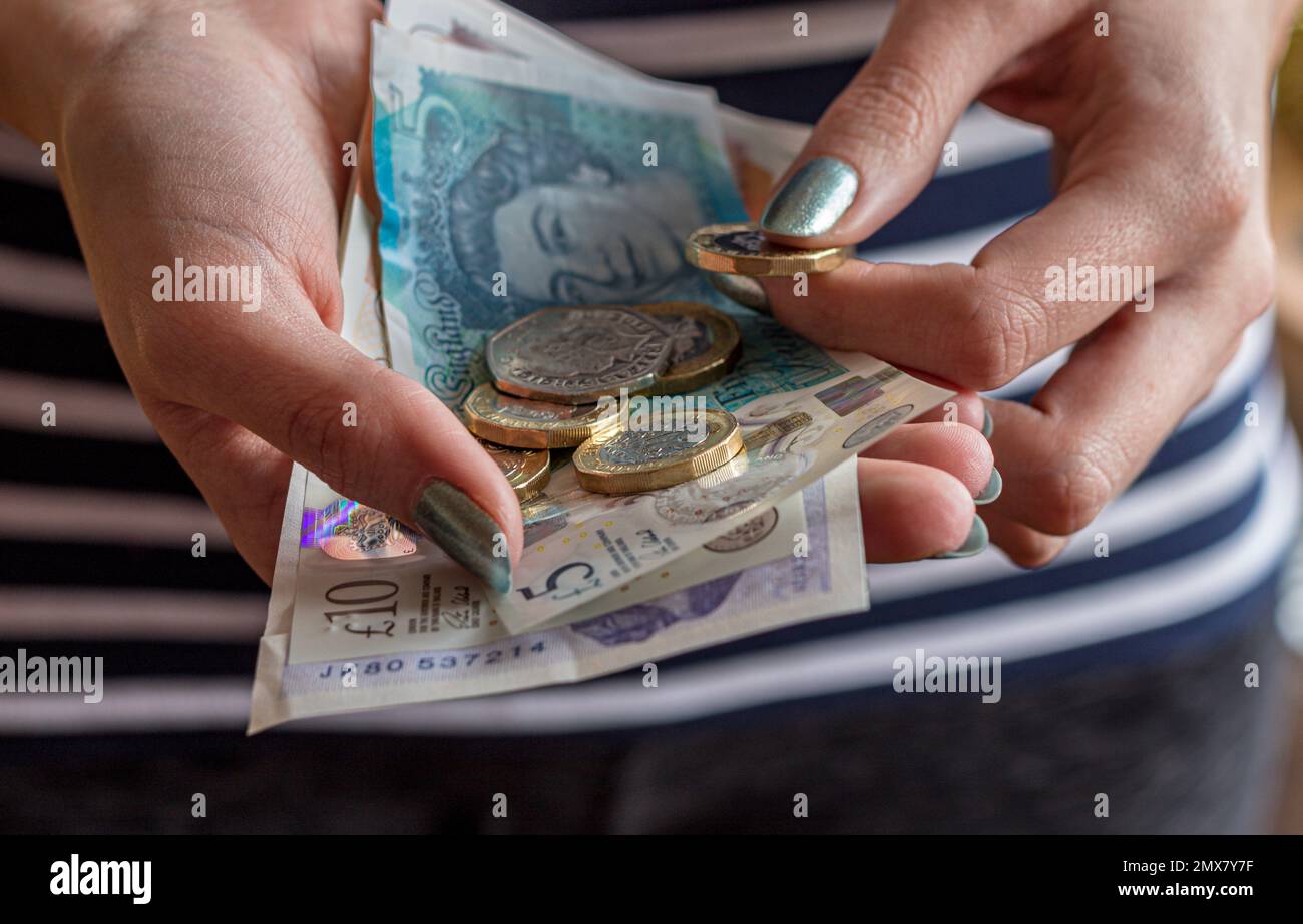 Primo piano delle mani di una donna in possesso di contanti, con banconote e monete di varie denominazioni di valuta britannica. Foto Stock