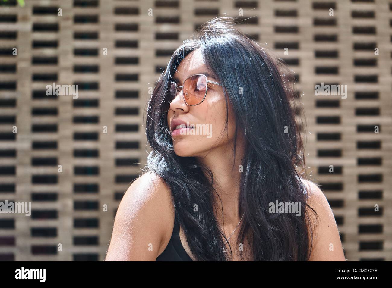 Modello femminile etnico a tutta lunghezza in occhiali da sole con capelli lunghi che guardano lontano e pensano mentre si rilassano sulla strada Foto Stock