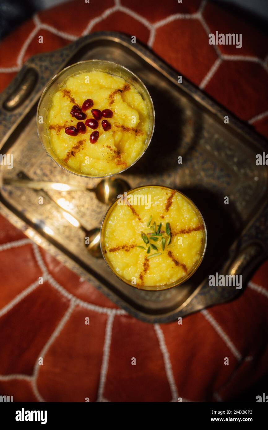 Due porzioni di Zarda Sholeh, un budino di riso allo zafferano persiano, dessert con cannella, melograno e guarnitura al pistacchio Foto Stock