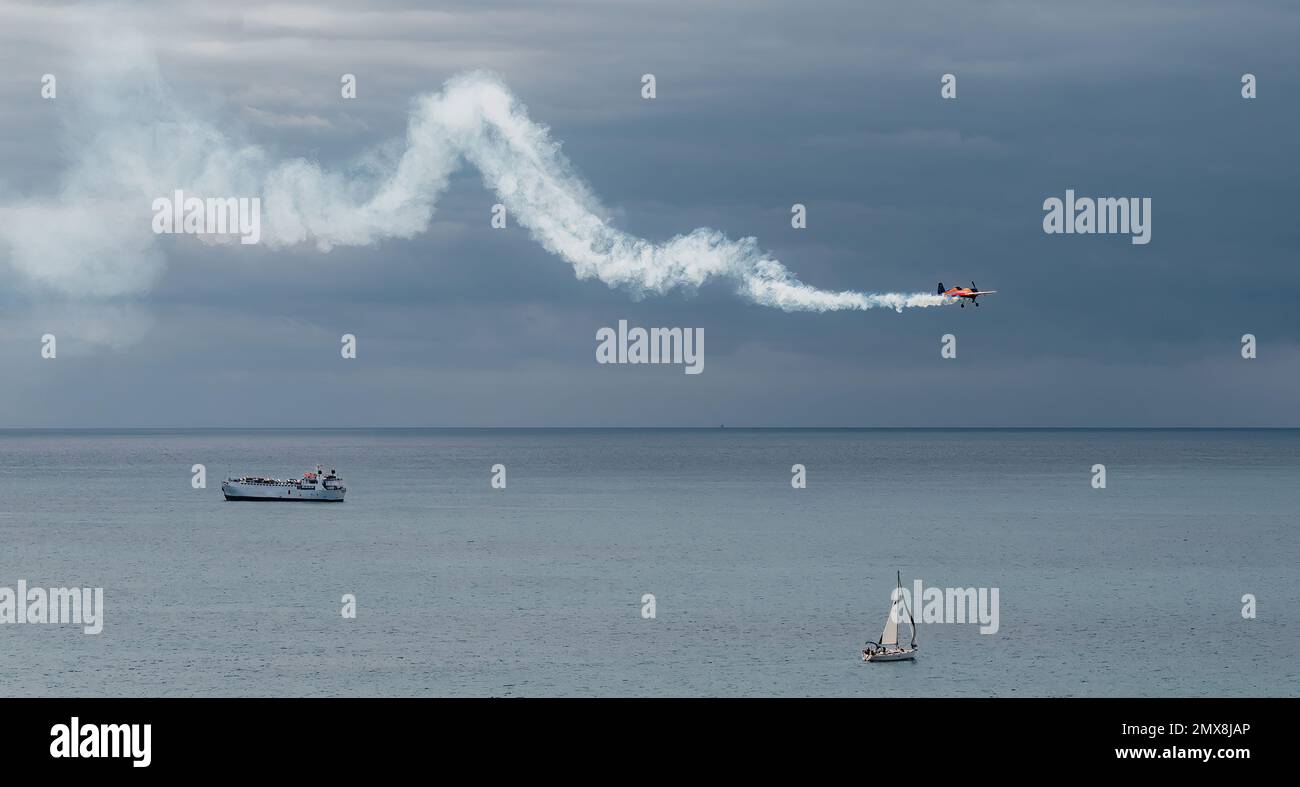 un velivolo leggero vola sul mare lasciando una traccia di fumo bianco. Foto Stock
