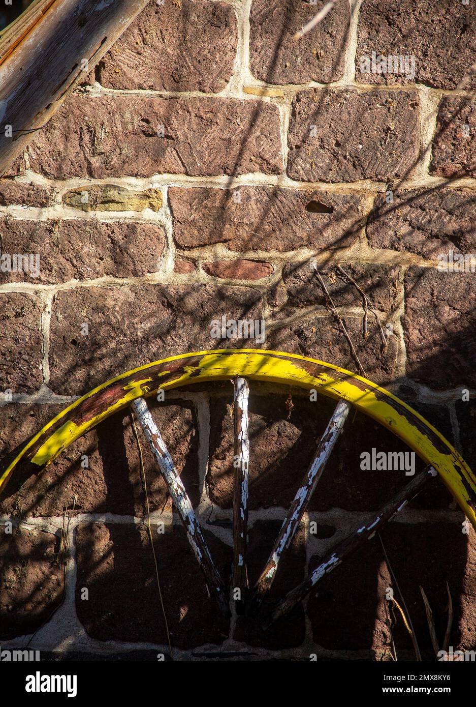 Vecchia ruota del carro contro un muro di pietra Foto Stock