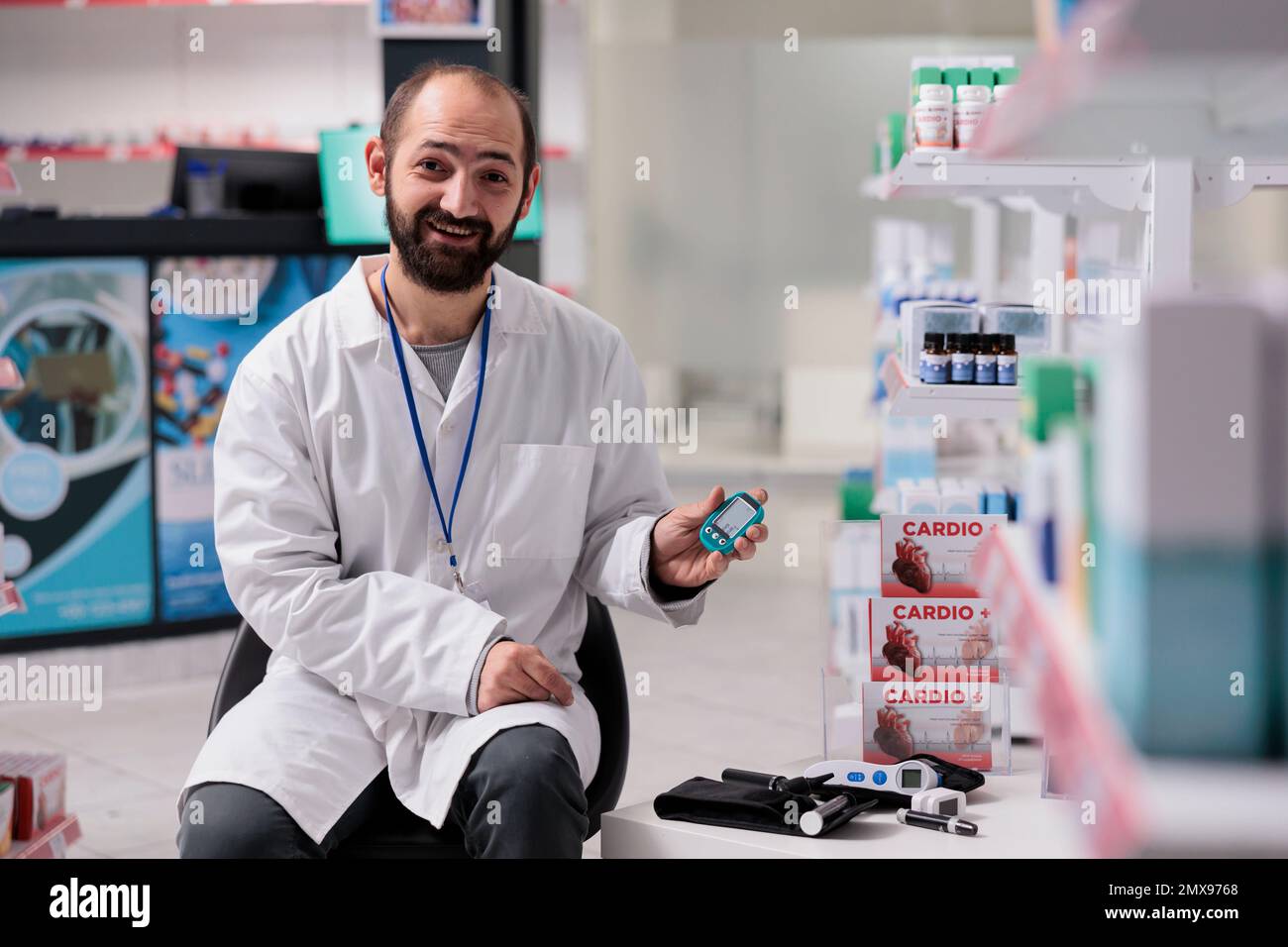 Farmacista in piedi sulla sedia in farmacia che tiene glucometro medico guardando la macchina fotografica mentre in attesa di clienti. Farmacia attrezzata con prodotti farmaceutici, vitamine e pillole Foto Stock