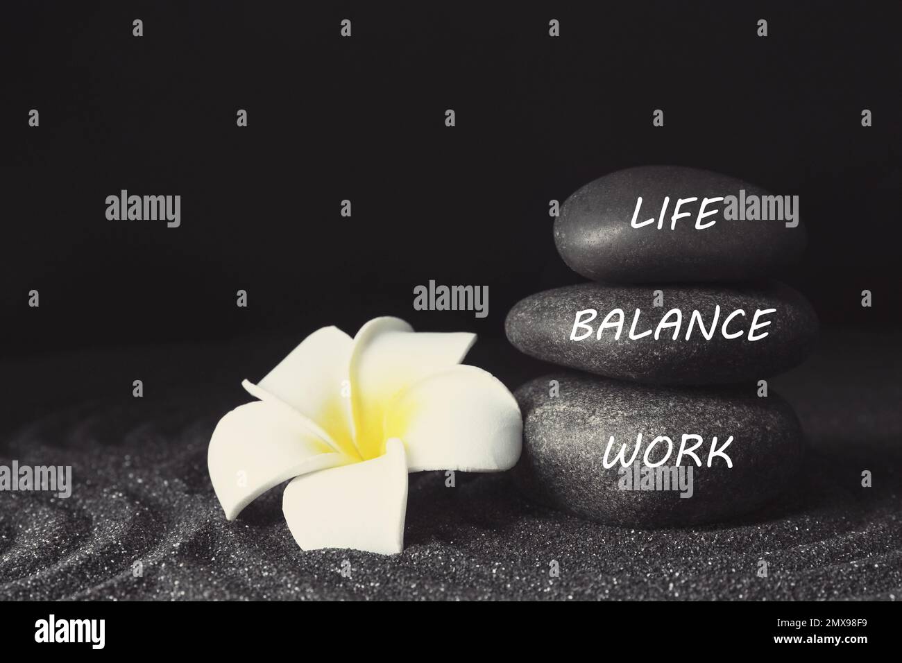 Concetto di equilibrio tra vita lavorativa e vita privata. Pietre impilate e fiori di plumeria sulla sabbia Foto Stock
