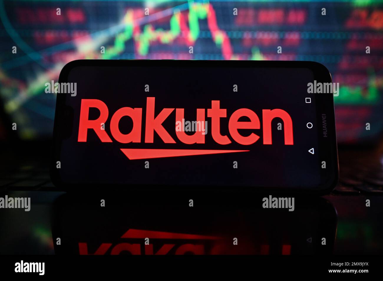 In questa illustrazione, un logo Rakuten viene visualizzato su uno smartphone con grafici di borsa sullo sfondo. Foto Stock