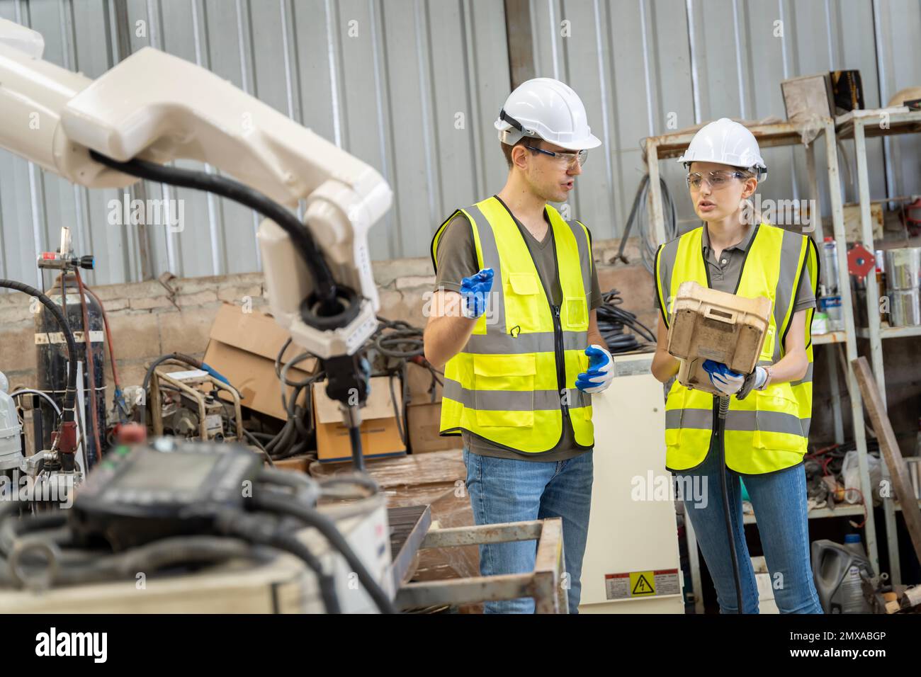 Un team di ingegneri maschili e femminili si riunisce per ispezionare i robot di saldatura dell'acciaio controllati dal computer. Pianificare le prove e l'installazione per l'uso. Foto Stock