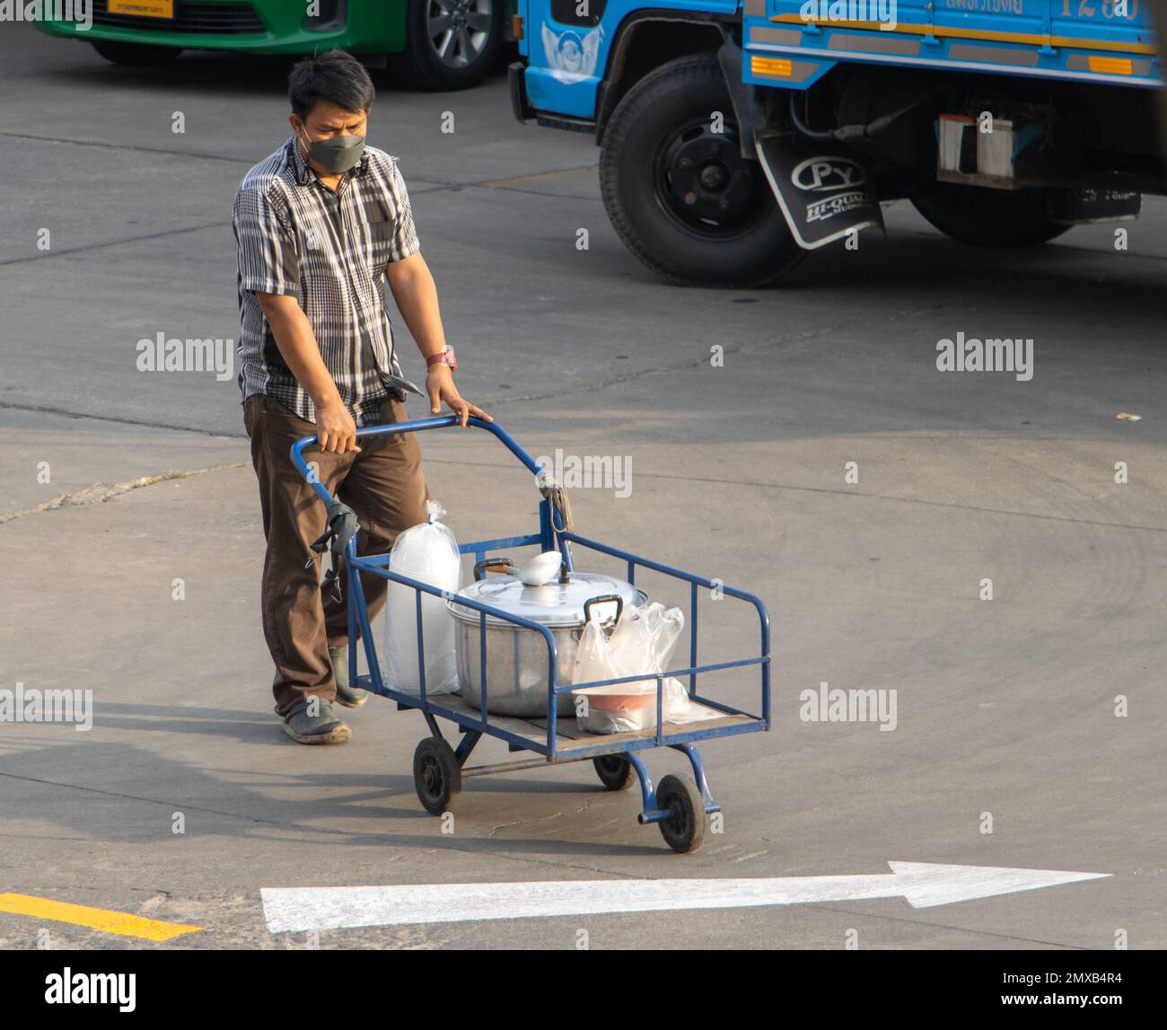 SAMUT PRAKAN, THAILANDIA, 30 2023 GENNAIO, Un uomo spinge un carrello a tre ruote con un carico Foto Stock