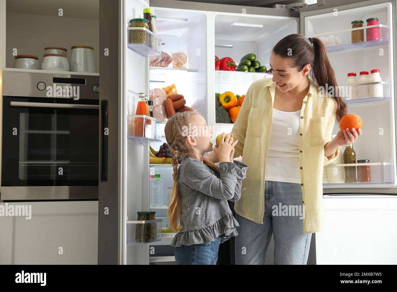 Giovane madre e sua figlia con frutta vicino frigorifero aperto in cucina  Foto stock - Alamy