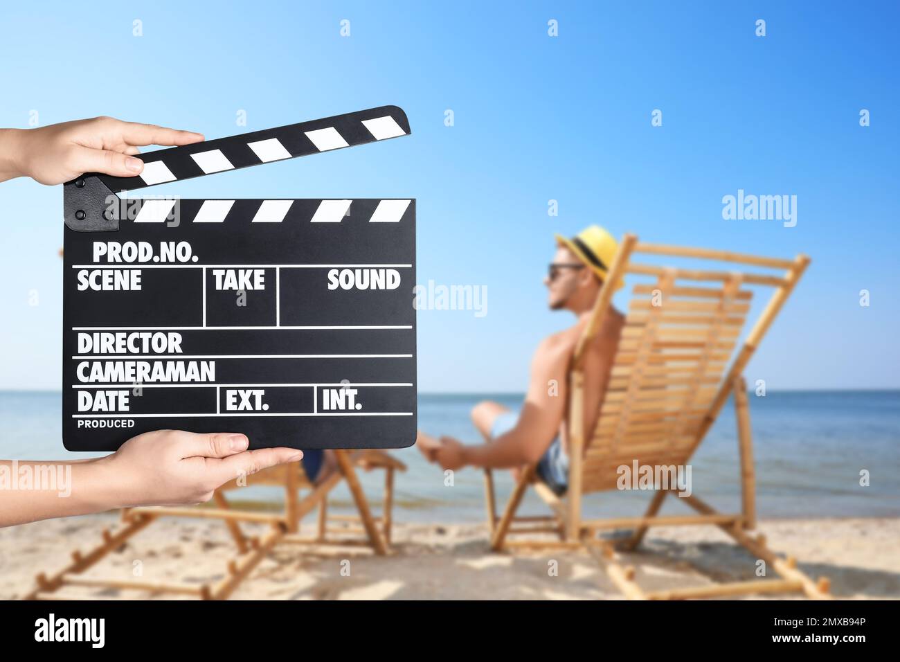 Assistente che tiene il clapperboard e le persone che si rilassano in sedie a sdraio sulla spiaggia, primo piano. Produzione cinematografica Foto Stock