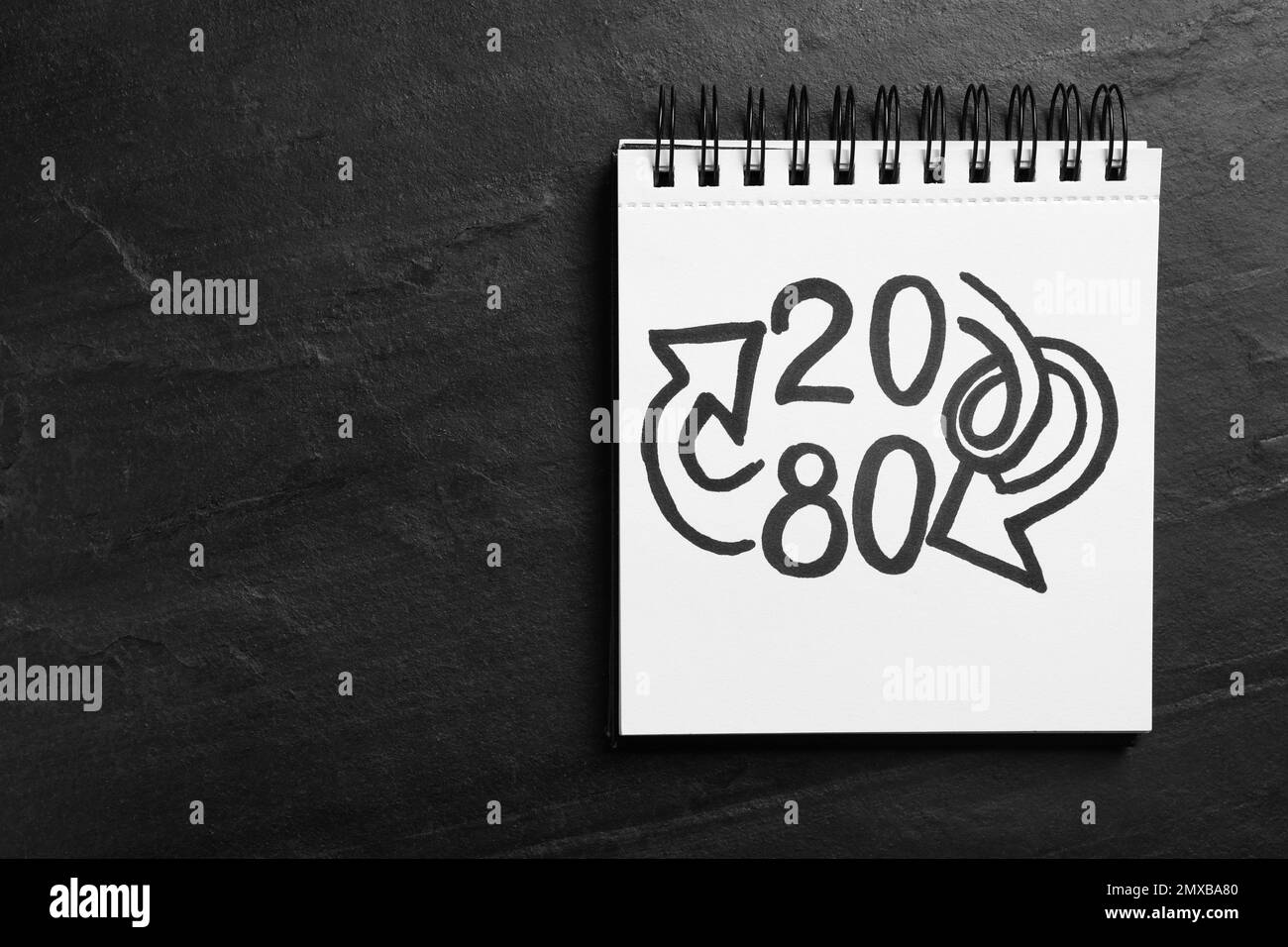 Vista dall'alto del notebook con i numeri 20, 80 e le frecce su sfondo nero ardesia, spazio per il testo. Principio di Pareto Foto Stock