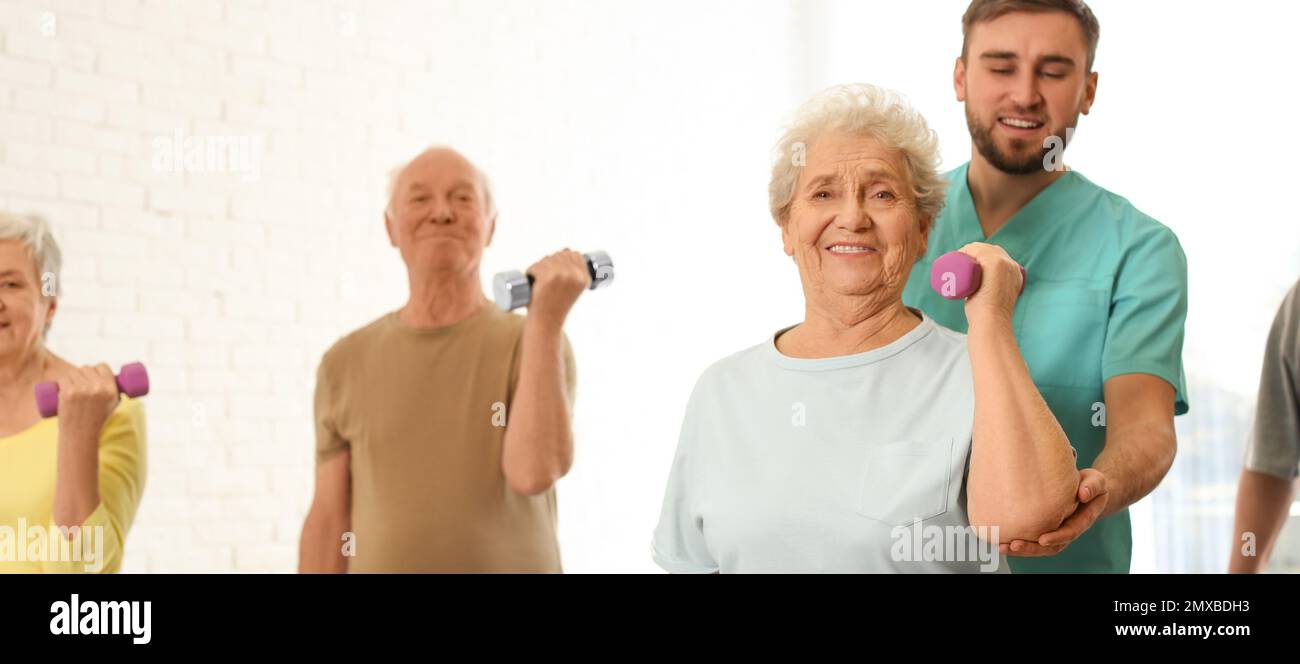 Assistente che aiuta la donna anziana a fare l'esercitazione con il dumbbell in palestra dell'ospedale. Design del banner Foto Stock