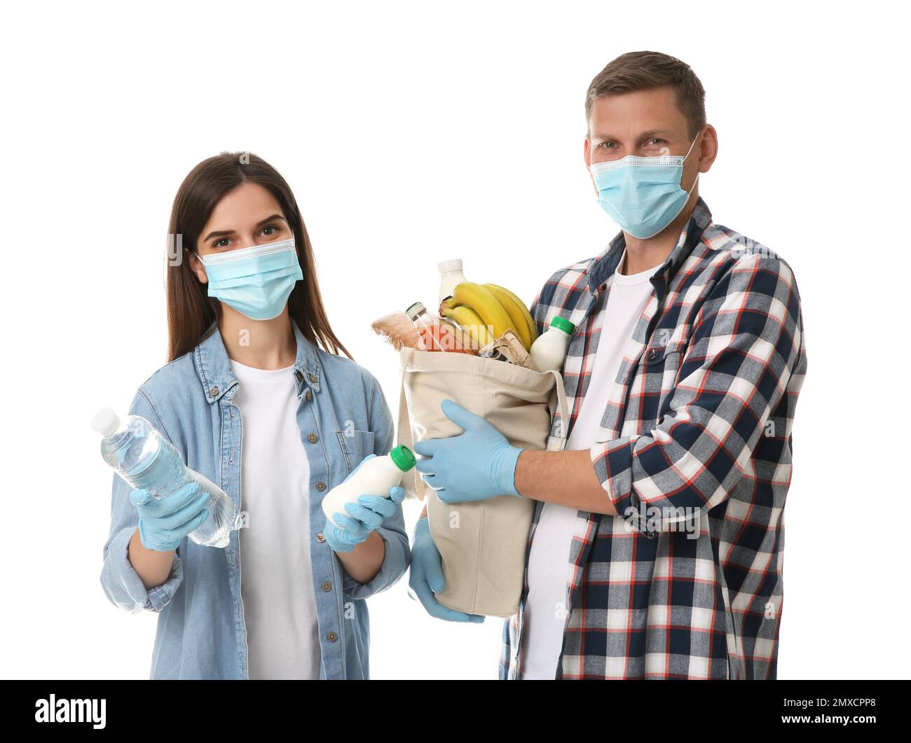 Volontari in maschere protettive e guanti con prodotti su sfondo bianco. Aiuto durante la quarantena del coronavirus Foto Stock