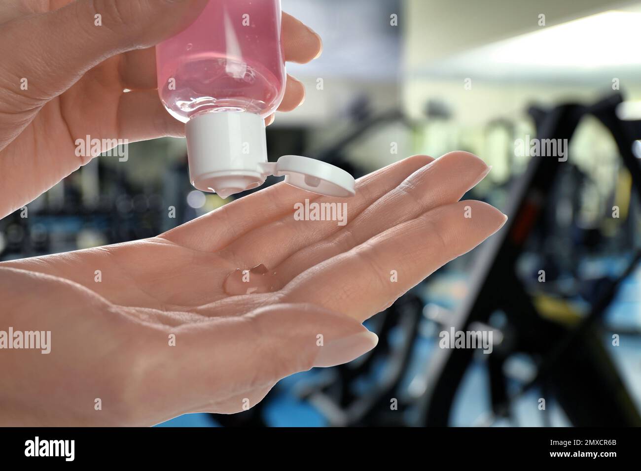 Donna che applica gel antisettico in palestra, primo piano. Misure preventive durante il periodo epidemico Foto Stock