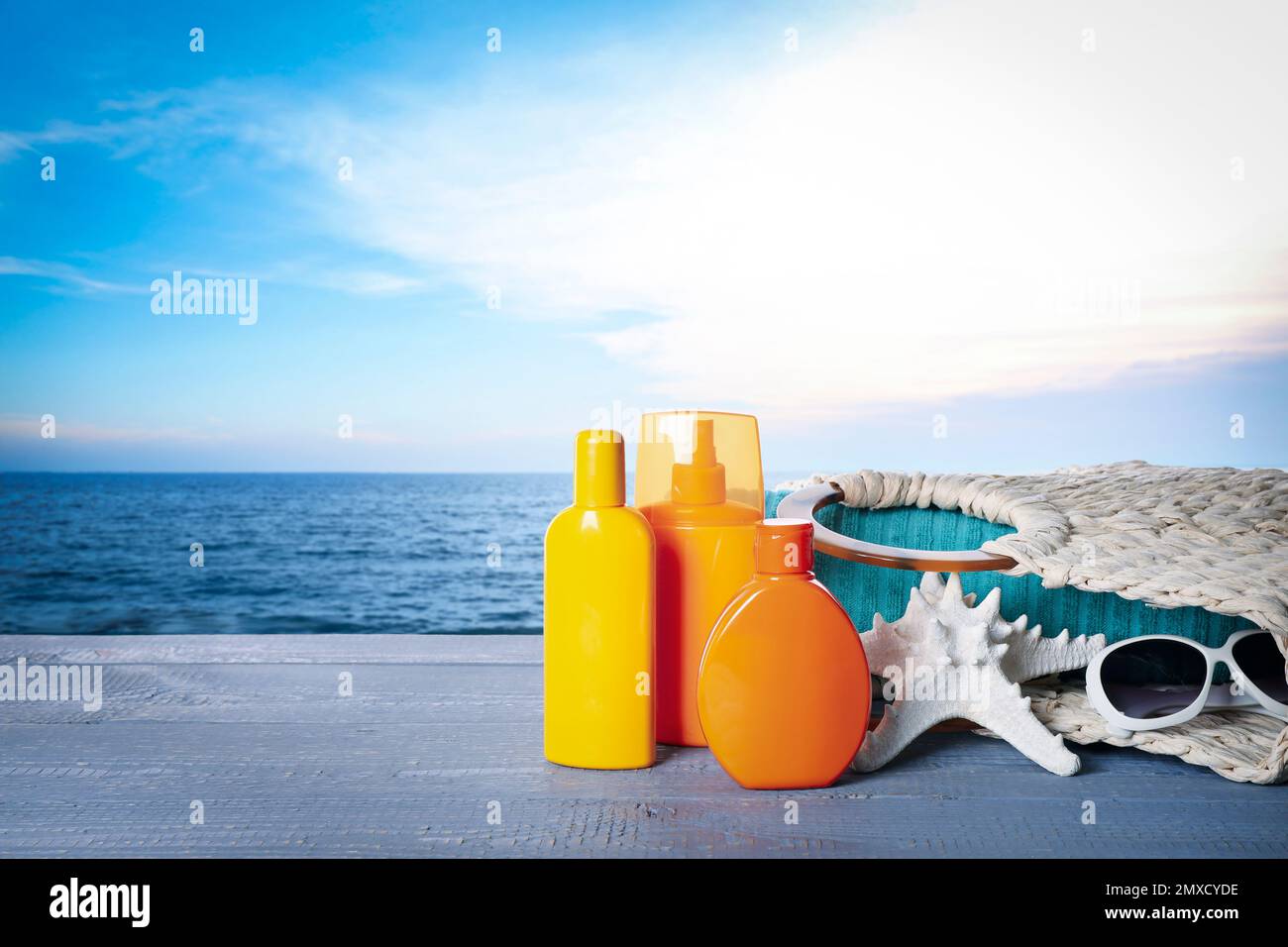 Set di prodotti per la protezione solare e accessori eleganti su tavola in legno vicino al mare. Spazio per il testo Foto Stock